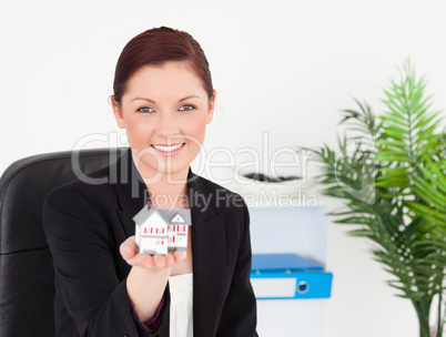 Young pretty red-haired woman in suit holding a miniature house