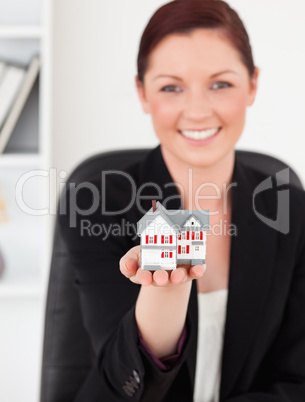 Young gorgeous red-haired woman in suit holding a miniature hous