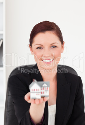 Attractive red-haired woman in suit holding a miniature house