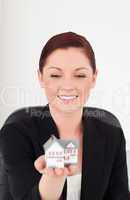 Good looking red-haired woman in suit holding a miniature house
