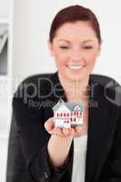 Beautiful red-haired woman in suit holding a miniature house