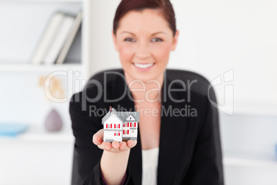 Pretty red-haired woman in suit holding a miniature house