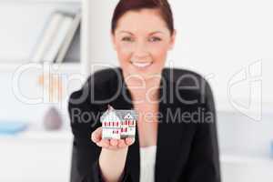 Pretty red-haired woman in suit holding a miniature house