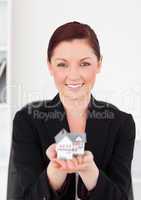 Cute red-haired woman in suit holding a miniature house