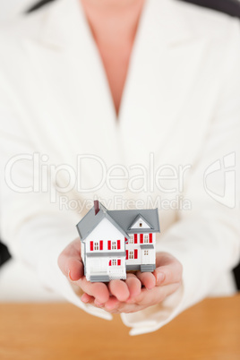 Young pretty red-haired female in suit holding a miniature house