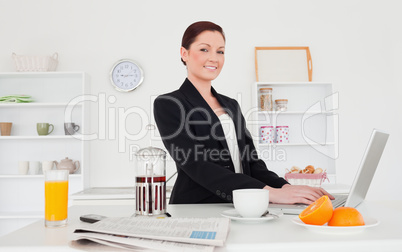 Good looking red-haired female in suit relaxing with her laptop