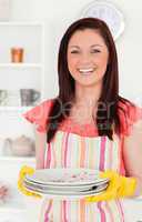 Beautiful red-haired woman holding some dirty plates in the kitc