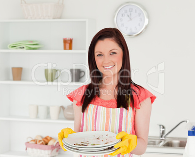 Attractive red-haired woman holding some dirty plates in the kit