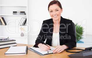 Beautiful red-haired female in suit writing on a notepad and pos