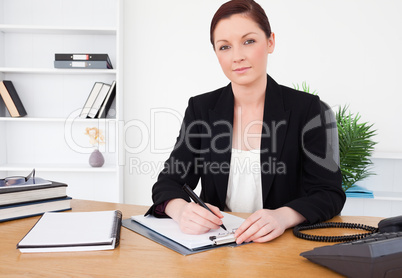 Attractive red-haired female in suit writing on a notepad and po