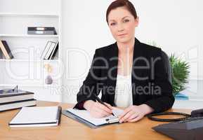 Attractive red-haired female in suit writing on a notepad and po