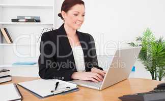 Young attractive red-haired female in suit typing on her laptop