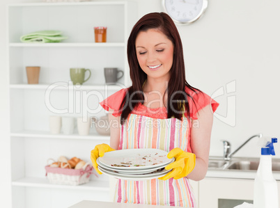 Good looking red-haired woman holding some dirty plates in the k