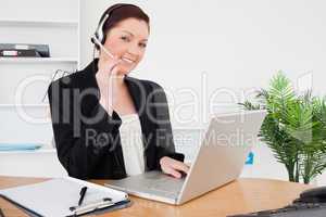 Young attractive red-haired female in suit typing on her laptop