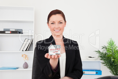 Young gorgeous red-haired female in suit holding a miniature hou