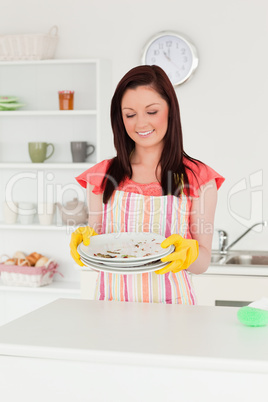 Pretty red-haired woman holding some dirty plates in the kitchen