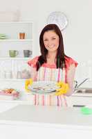 Gorgeous red-haired woman holding some dirty plates in the kitch