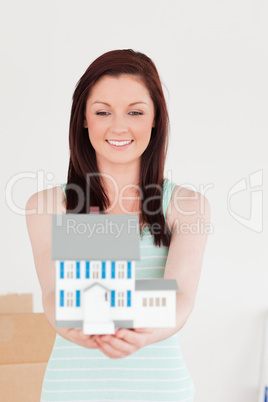 Good looking red-haired woman holding a miniature house while st