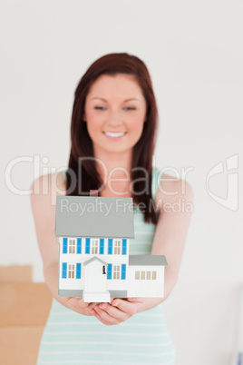 Pretty red-haired woman holding a miniature house while standing