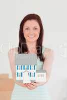 Cute red-haired woman holding a miniature house while standing o