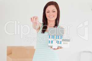 Pretty red-haired female holding a miniature house while standin