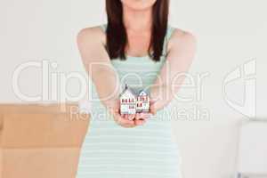 Cute red-haired female holding a miniature house while standing