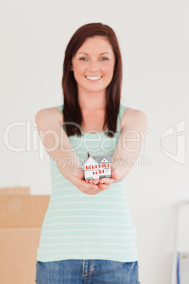 Gorgeous red-haired female holding a miniature house while stand