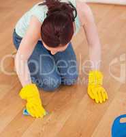Attractive red-haired woman cleaning the floor while kneeling