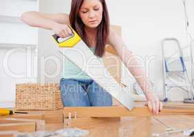 Beautiful red-haired female using a saw for diy at home