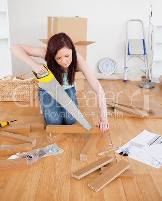 Attractive red-haired female using a saw for diy at home