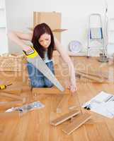 Attractive red-haired female using a saw for diy at home