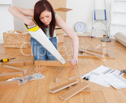 Good looking red-haired female using a saw for diy at home
