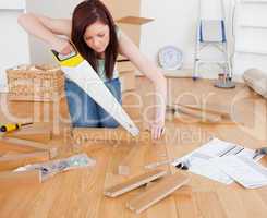 Good looking red-haired female using a saw for diy at home