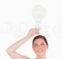 Gorgeous red-haired woman holding a bulb while standing