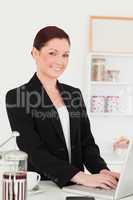 Pretty red-haired woman in suit relaxing with her laptop in the