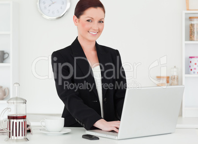Pretty red-haired woman in suit relaxing with her laptop while p