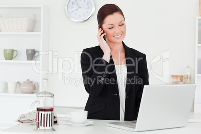 Pretty red-haired woman in suit relaxing with her laptop while p