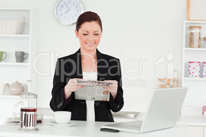 Pretty red-haired woman in suit reading the newspaper in the kit