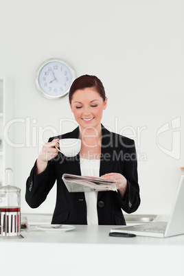 Good looking red-haired woman in suit reading the newspaper whil