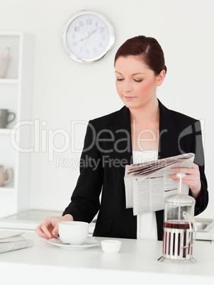 Gorgeous red-haired woman in suit reading the newspaper in the k