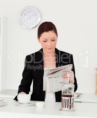 Pretty red-haired woman in suit reading the newspaper in the kit