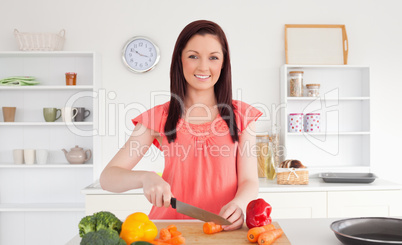 Beautiful red-haired woman cutting some vegetables in the kitche