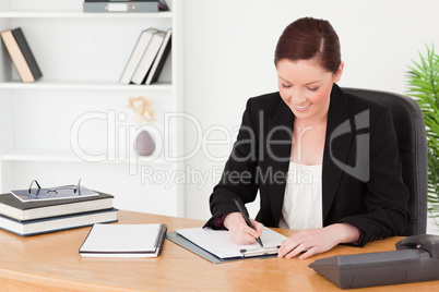 Beautiful red-haired woman in suit writing on a notepad