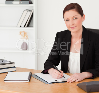 Good looking red-haired woman in suit writing on a notepad