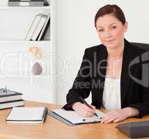 Good looking red-haired woman in suit writing on a notepad