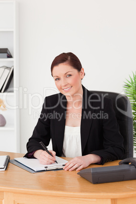 Beautiful red-haired woman in suit writing on a notepad and posi