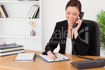 Beautiful red-haired woman in suit writing on a notepad and phon