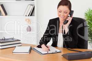 Beautiful red-haired woman in suit writing on a notepad and phon