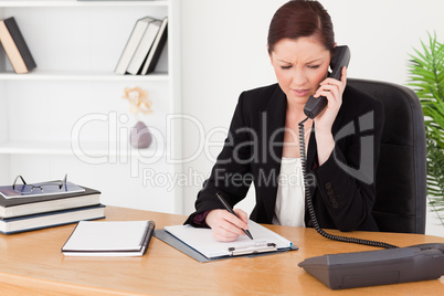 Attractive red-haired woman in suit writing on a notepad and pho Attractive red-haired woman in suit writing on a notepad and pho