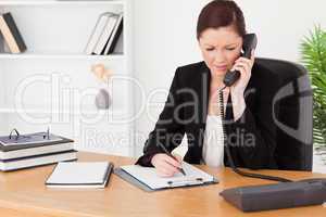 Attractive red-haired woman in suit writing on a notepad and pho